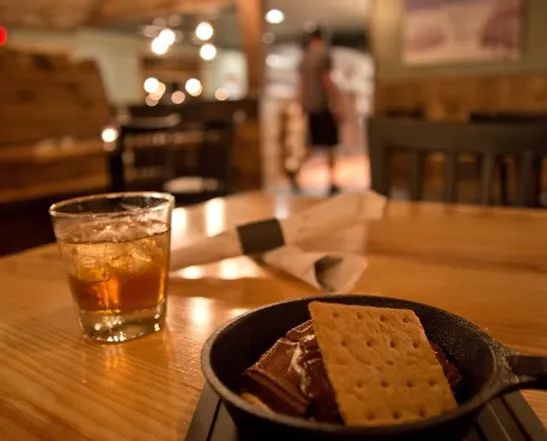 small cast iron pan with a dessert on a restaurant table with a glass of whiskey 
